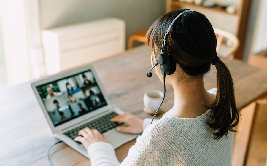 白いセーターを着た女性が城下工業サウンドウォーリアの片耳ヘッドセットSW-H1をつけてノートパソコンの前にすわりオンライン会議をしている