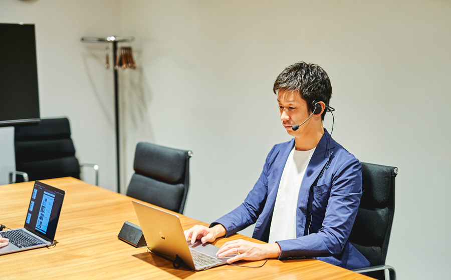 男性がオフィスで城下工業サウンドウォーリアの片耳スピーカーの折りたたみできるヘッドセットSW-HW2をつけてノートパソコンの前にすわっている