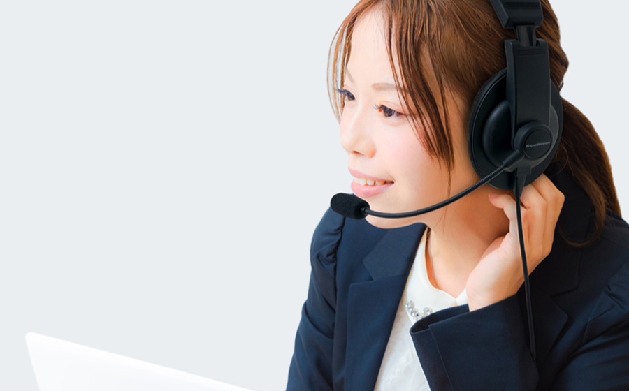 紺色のジャケットをきた女性が片耳タイプのオーバーヘッドのSOUND WARRIORヘッドセットSW-TR1をつけてパソコンの前で会話している