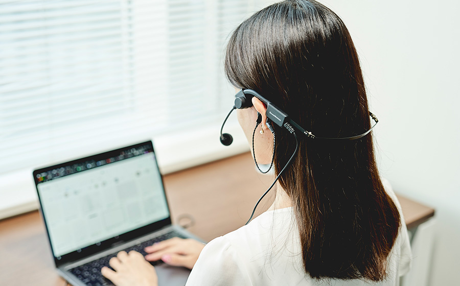 城下工業SOUND WARRIORヘッドセットはイヤホンを差し込んで使うタイプで、ヘッドセットをつけて女性がコワーキングスペースでパソコンをしている