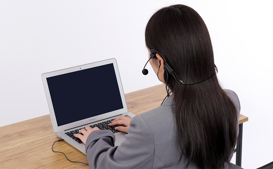 城下工業SOUND WARRIORヘッドセットはイヤホンを差し込んで使うタイプで、ヘッドセットをつけて女性がコワーキングスペースでパソコンをしている