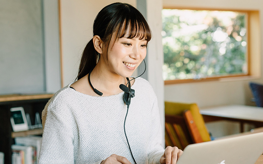 城下工業SOUND WARRIORネックセットSW-NS1を白いセーターを着た女性がヘッドセットをしてパソコンでオンライン会議をしている